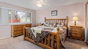 A bedroom with a wooden bed, a ceiling fan, a window, and a nightstand with a lamp. - Family 4BR Home With Patio by Willowcreek Park (Sparks)