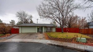 A single-story house with a front garage, a small front yard, and a red fence. - Family 4BR Home With Patio by Willowcreek Park (Sparks)