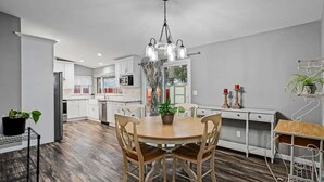 A modern kitchen with white cabinets, a wooden dining table, and a hanging light fixture. - Family 4BR Home With Patio by Willowcreek Park (Sparks)