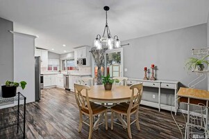 Una cocina moderna con armarios blancos, una mesa de comedor de madera y una lámpara colgante.