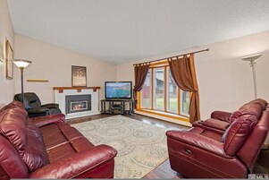 A living room with a fireplace, leather sofas, a television, and a large window with curtains.
