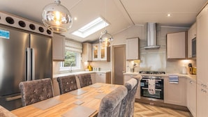 A modern kitchen with a dining area, featuring a large refrigerator, oven, and a dining table with chairs. - Host Stay Lakeside Retreat (York)