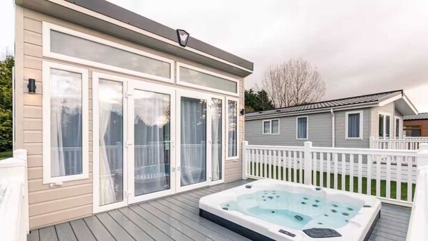 A deck with a hot tub, a house with large windows, and a white fence. - Host Stay Lakeside Retreat (York)