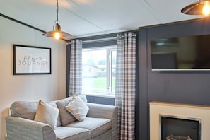 A living room with a grey sofa, a fireplace, a television, and a window with curtains. - Host Stay Lotus Lodge (York)