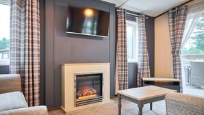 A modern living room with a fireplace, a flat-screen TV mounted above it, and a dining area with a table and chairs. - Host Stay Lotus Lodge (York)