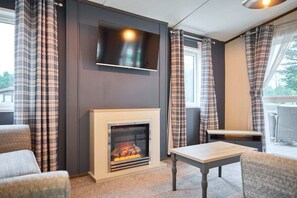 A modern living room with a fireplace, a flat-screen TV mounted above it, and a dining area with a table and chairs. - Host Stay Lotus Lodge (York)