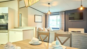 A modern kitchen with a microwave, a dining table set with white plates and cups, and a living area with a sofa and a TV. - Host Stay Lotus Lodge (York)