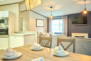 A modern kitchen with a microwave, a dining table set with white plates and cups, and a living area with a sofa and a TV. - Host Stay Lotus Lodge (York)
