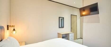 Habitación de hotel con cama, escritorio, espejo y televisor de pantalla plana montado en la pared.