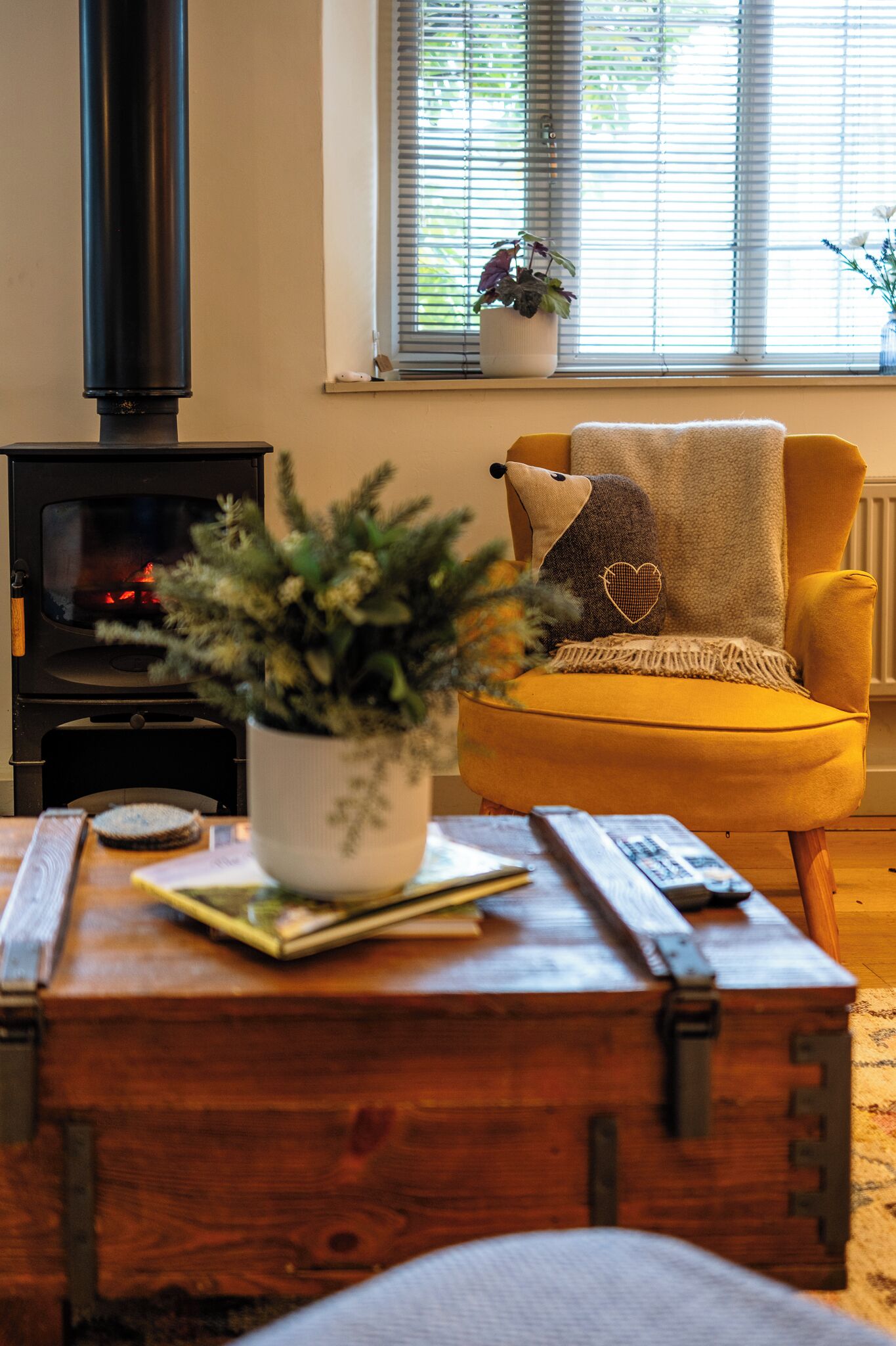 A cozy living room with a yellow armchair, a white potted plant, and a wooden chest of drawers.