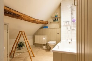 A bathroom with a wooden ceiling beam, a white radiator, a toilet, a sink, and shelves with toiletries. - Beautiful Cottage in the Cotswolds (Chipping Campden)
