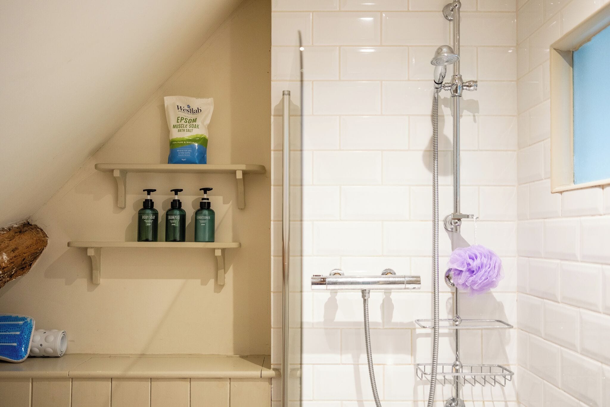 A bathroom with a shower, a shelf with toiletries, and a window.