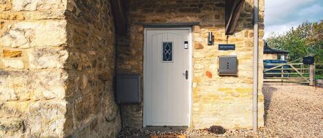 Ein Steingebäude mit einer weißen Tür, einer Fußmatte und einem Schild mit der Aufschrift 'Brew Cottage'.