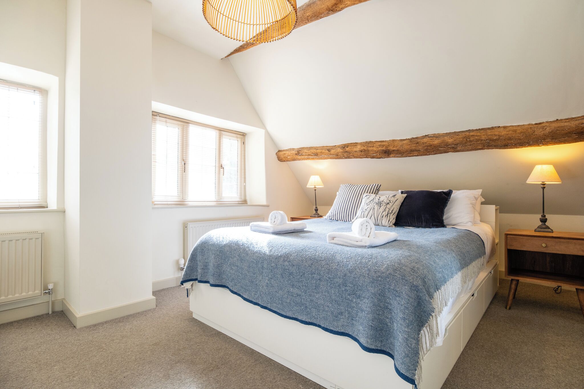 A bedroom with a bed, two bedside lamps, a window, and a radiator.