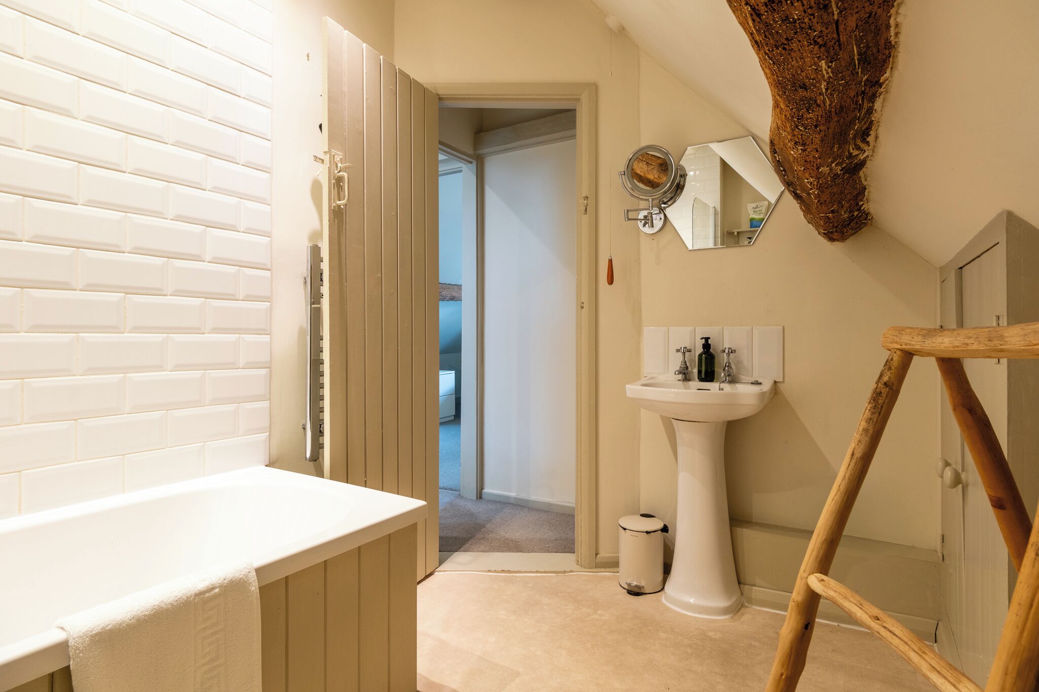 Une salle de bain avec une baignoire blanche, un lavabo sur colonne et une échelle en bois.