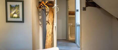 A hotel room with a wooden beam ceiling, a framed picture on the wall, and a hallway leading to another room.