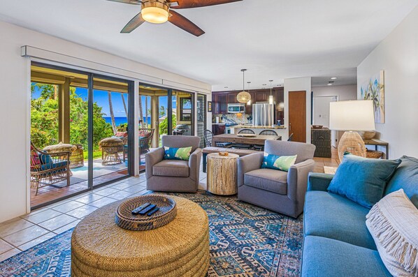 A spacious living area with a large sofa, two armchairs, a coffee table, and a dining table. There is a kitchen in the background with modern appliances and a large window offering a view of the outdoors. - SUMMER SALE! Hillside Condo w/ AC & Ocean Views Near Beaches-Wailea Ekolu 1605 (Kihei)