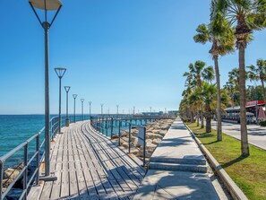 A wooden boardwalk along a coastal area with street lamps, palm trees, and a clear blue sky. - Sanders Soul Apartments - Full Building (Limassol)