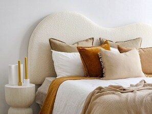 A bed with a textured headboard, multiple pillows, a bedside table with candles, and a blanket. - Sanders Soul Apartments - Full Building (Limassol)
