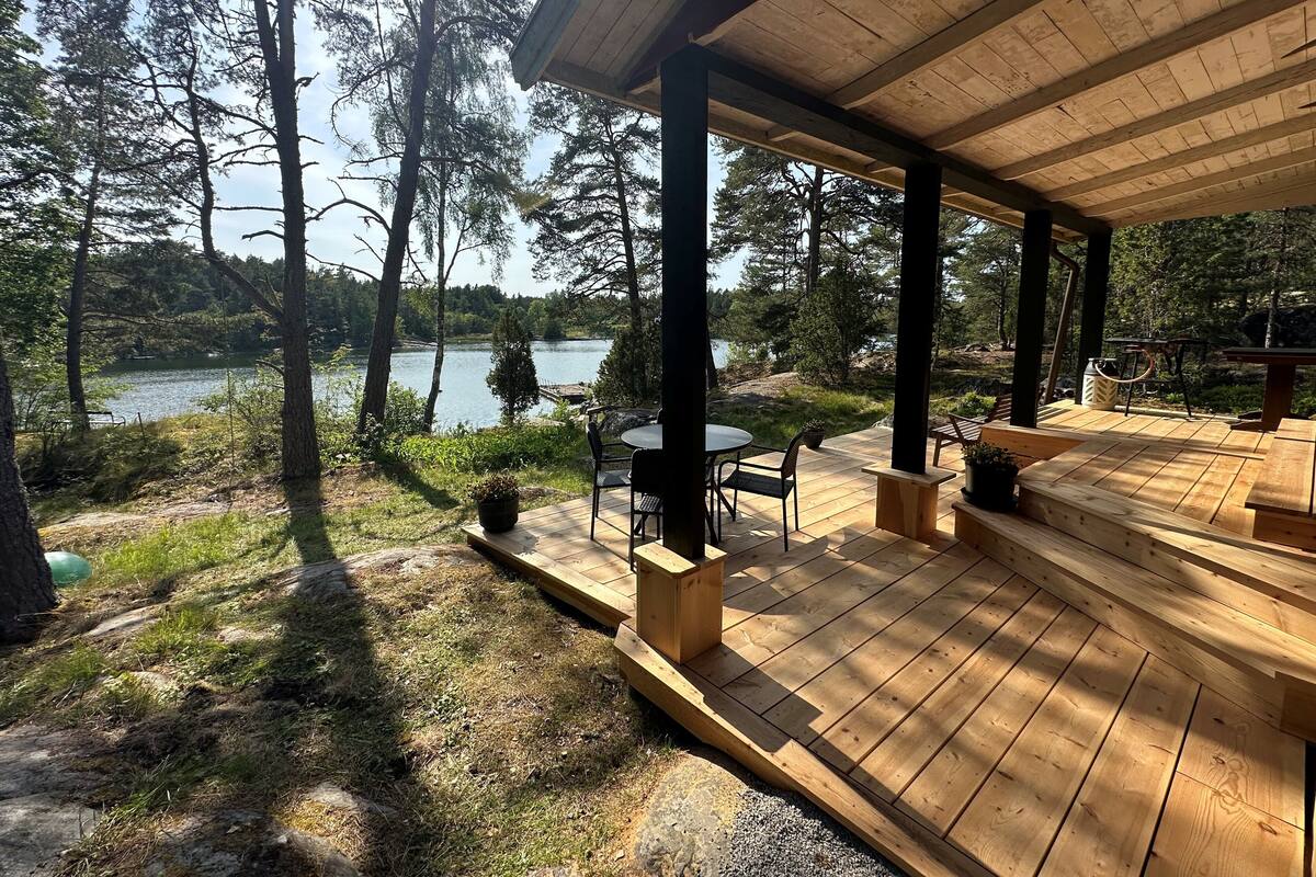 A wooden deck with a table and chairs, overlooking a lake surrounded by trees.