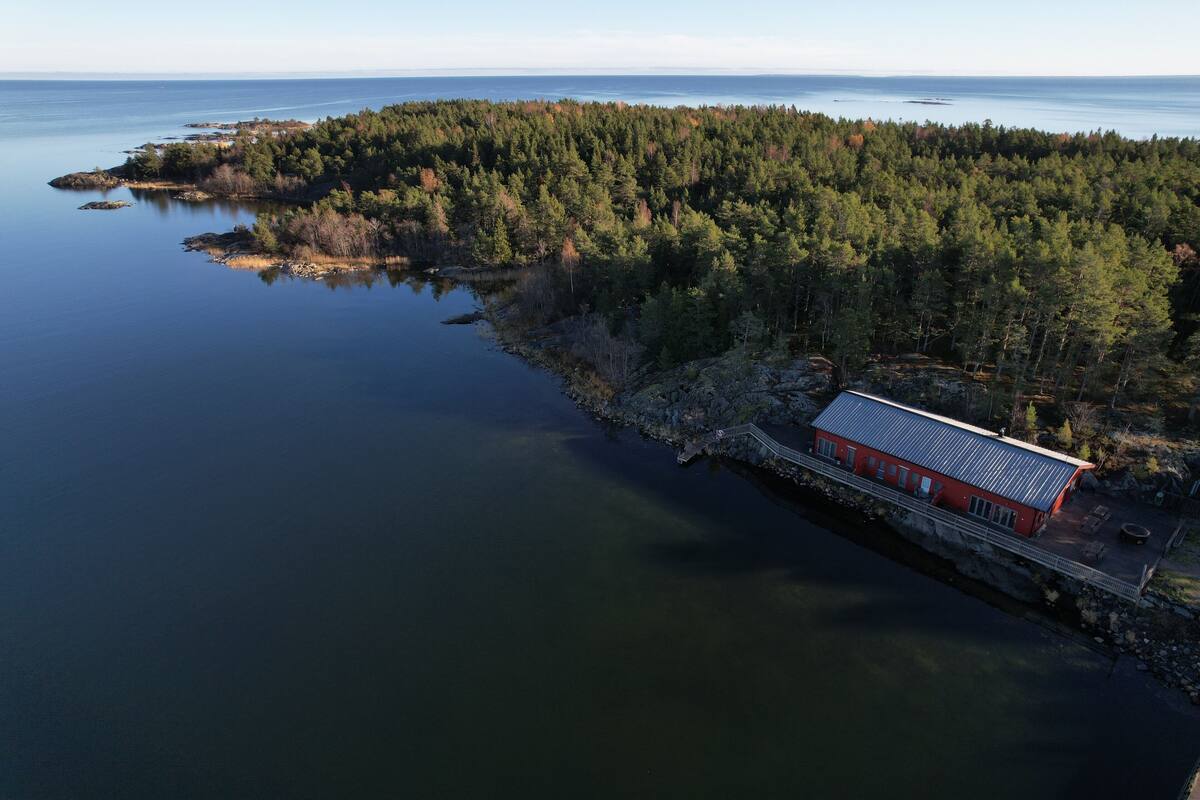 An aerial view of a coastal property with a red building, surrounded by dense forest and a calm body of water.