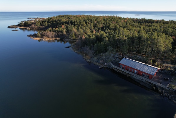 An aerial view of a coastal property with a red building, surrounded by dense forest and a calm body of water.