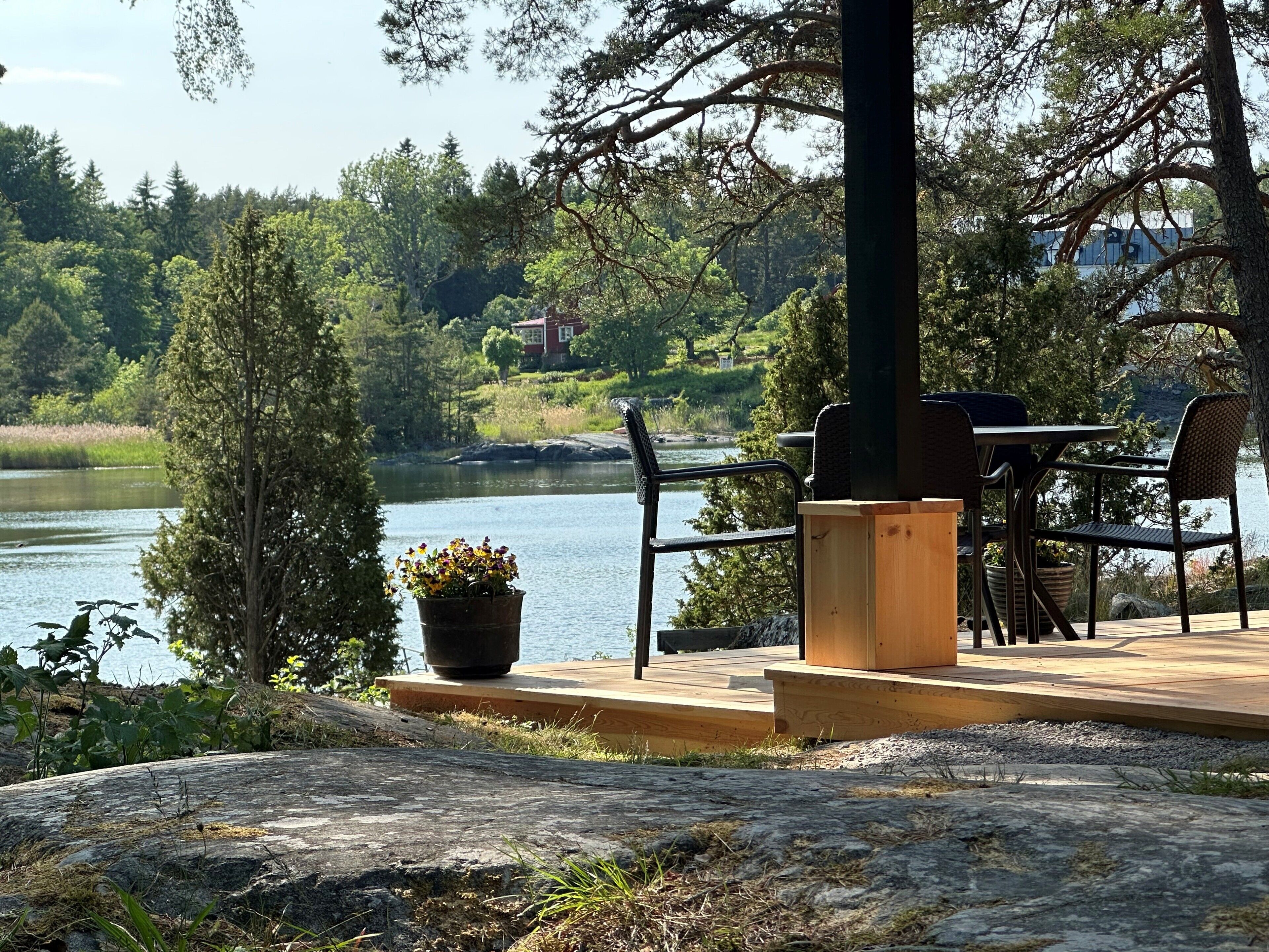 Un patio junto al lago con una mesa y sillas, un banco de madera y una planta en maceta.