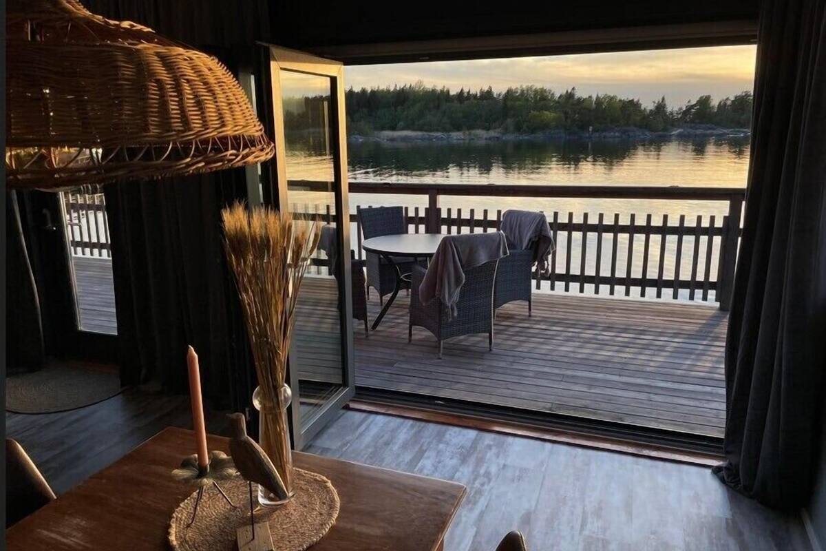 A room with a view of a lake, a dining table with chairs, and a wicker chair.