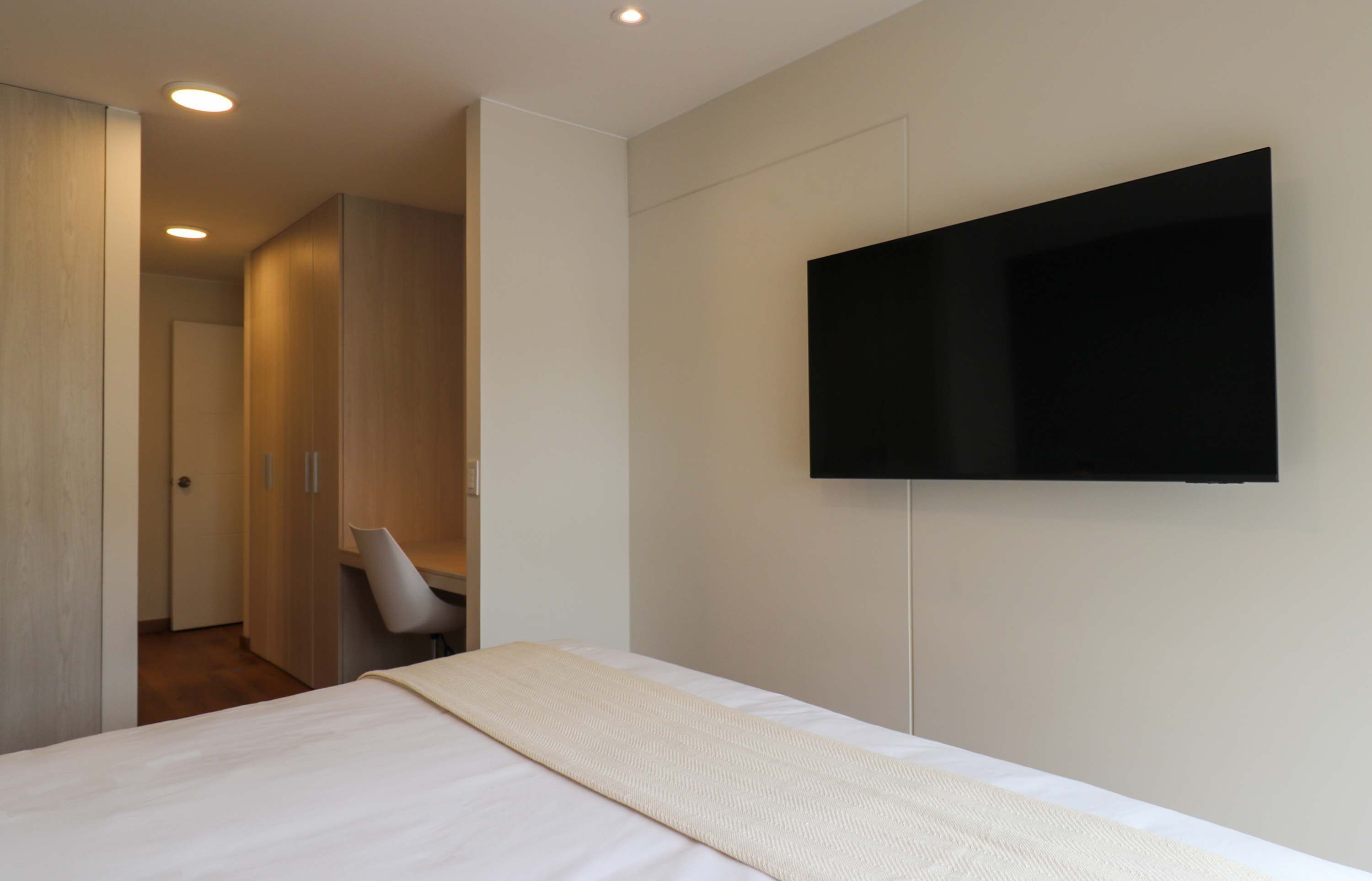 A modern bedroom with a bed, a TV mounted on the wall, and a chair.