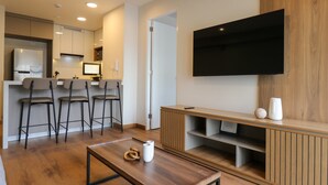 A modern living room with a wooden coffee table, a TV mounted on the wall, and a kitchen area with bar stools. - w Lovely 2BR w Balcony in Miraflores (Lima)
