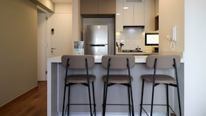 A modern kitchen with a stainless steel refrigerator, a built-in oven, and a microwave. There are three bar stools and a white countertop. - w Lovely 2BR w Balcony in Miraflores (Lima)