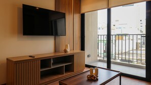 A modern living room with a flat-screen TV mounted on the wall, a wooden entertainment unit, and a large window offering a view of the city. - w Lovely 2BR w Balcony in Miraflores (Lima)