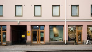 A building with a pink facade, a ground-floor entrance with a door, and a storefront with glass windows displaying artwork. - Beautiful Studio in Middle of Downtown (Turku)