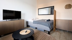 A modern hotel room with a bed, a TV, a small table, and a large mirror. - Beautiful Studio in Middle of Downtown (Turku)