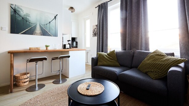 A modern living room with a sofa, a coffee table, and a dining area with a counter and stools. - Beautiful Studio in Middle of Downtown (Turku)