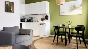 Une cuisine moderne avec des meubles blancs, un coin repas comprenant une table et des chaises, et un canapé gris.