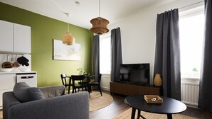 Un salon moderne avec un mur d’accent vert, un canapé, une table à manger et un téléviseur.