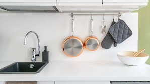 Une cuisine avec un évier, deux casseroles en cuivre, une marmite noire et une cuillère en bois dans un bol.