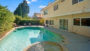 Un giardino con piscina, un patio con sedie e una casa con tetto in tegole.