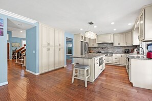 A spacious kitchen with white cabinetry, a granite countertop, and a central island with a stool. - Spacious 4BR Family Retreat w Private Pool (Cerritos)