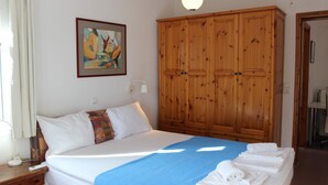 A hotel room with a bed, a blue blanket, a wooden wardrobe, a painting on the wall, and a window with curtains. - Couples Warm Nook - Thassos Seabreeze Nest (Thasos)