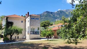 Un edificio de piedra con techo de tejas rojas, rodeado de árboles y un paisaje montañoso.