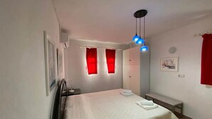 A bedroom with a bed, a bench, a wardrobe, and a ceiling light fixture. - Anatoli Garden View - Cozy Thassos Getaway (Thasos)