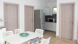 Una cucina compatta con frigorifero, forno a microonde e pensili bianchi. Si nota un tavolo da pranzo con sedie e una ciotola blu.