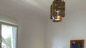 Camera d'albergo con un letto di legno, lenzuola bianche, un comodino, una lampada a parete e un quadro.