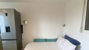 Una camera d'albergo piccola e moderna, con un letto, un tavolino e un frigorifero.