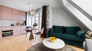 A modern kitchen with pink cabinets, a dining area with a round table and chairs, and a green sofa in a living space. - Dünenloft, House Kliff Whg. 11 (Sylt)