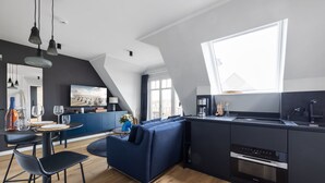 Een moderne keuken met een ingebouwde oven, een zithoek met een blauwe bank en een groot raam dat voor natuurlijk licht zorgt.