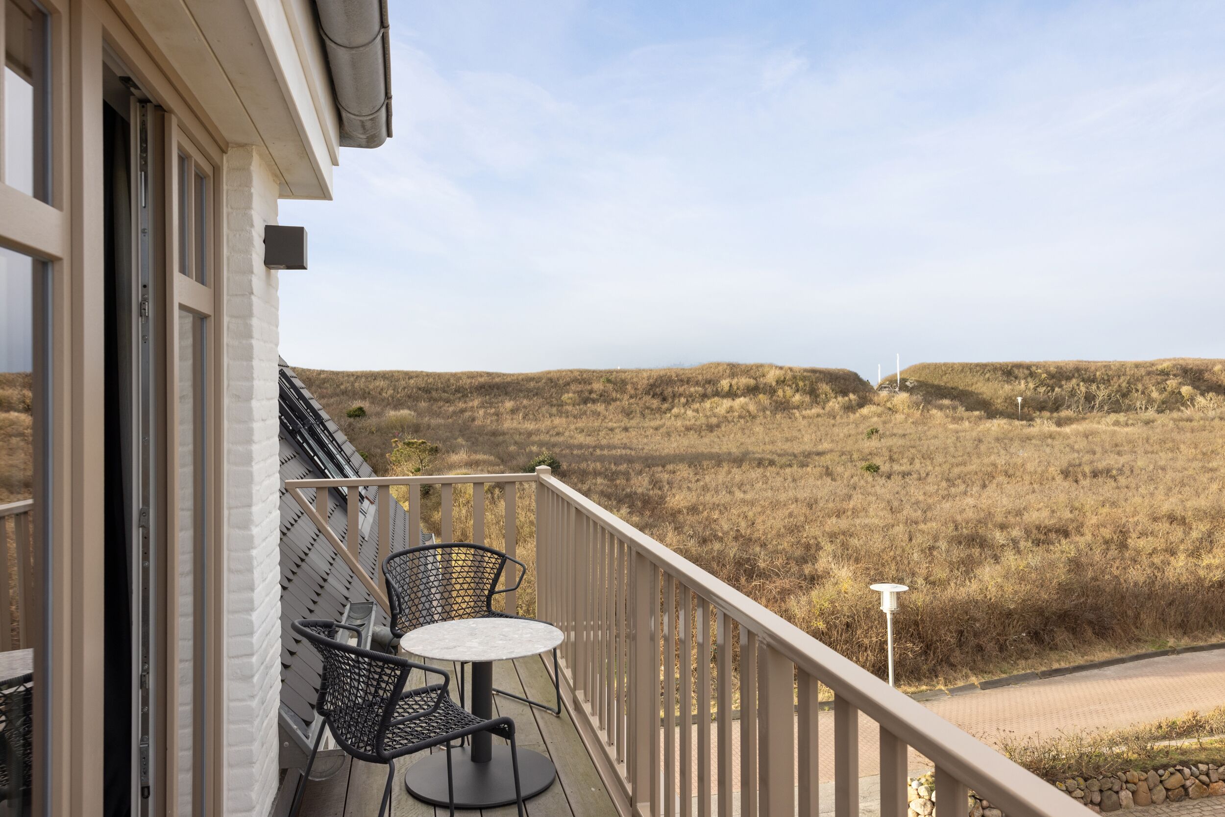 A balcony with two chairs and a table, overlooking a dry landscape with hills and a clear sky.