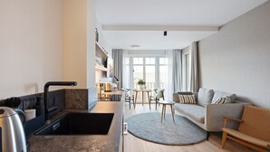 A modern kitchen with a built-in sink, a kettle, and a dining area with a round rug and a sofa. - Dünenloft, House Kliff Whg. 5 (Sylt)